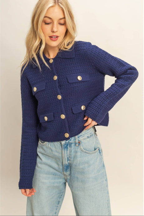 Woman wearing a blue textured jacket with gold buttons on a plain background