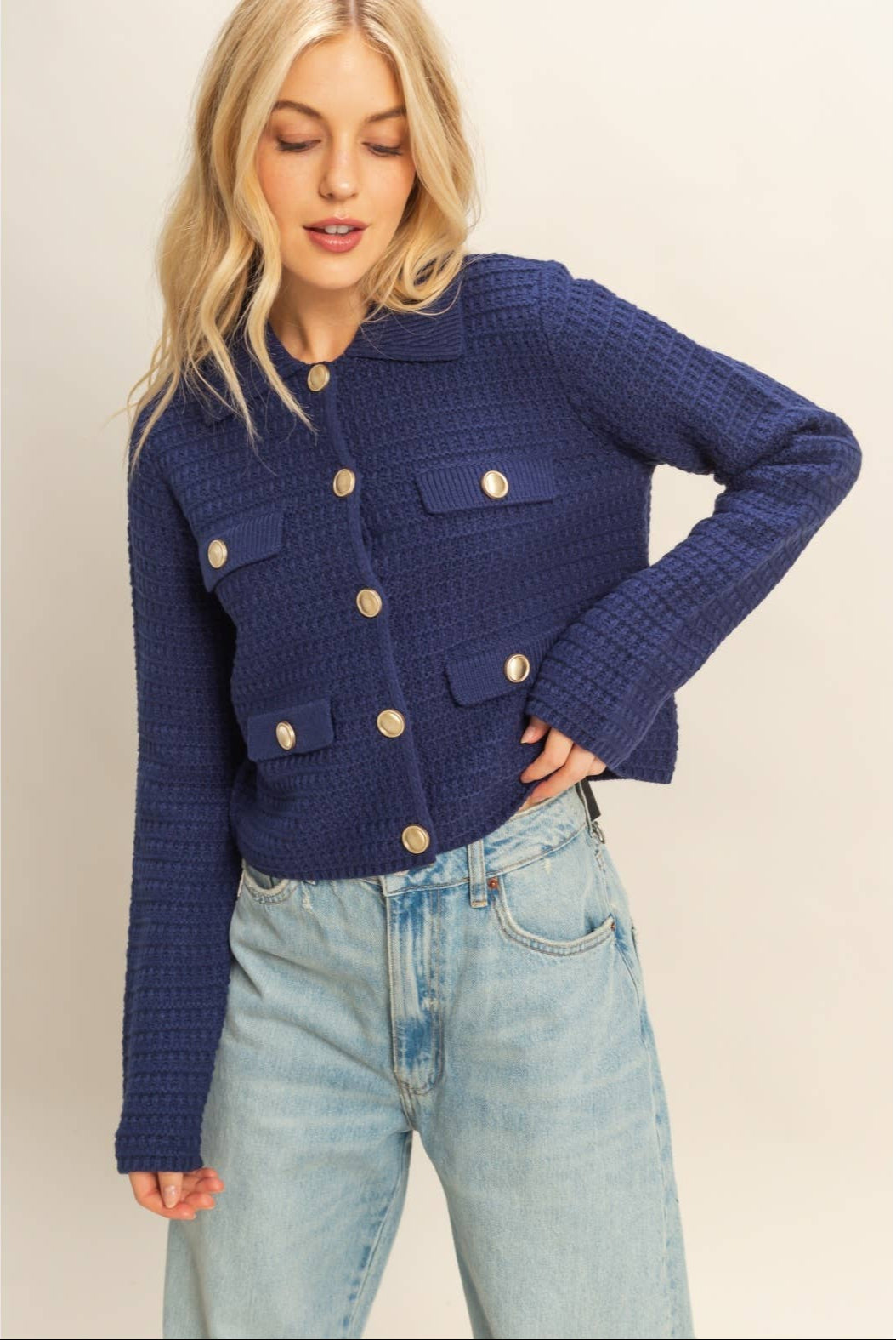 Woman wearing a blue textured jacket with gold buttons on a plain background