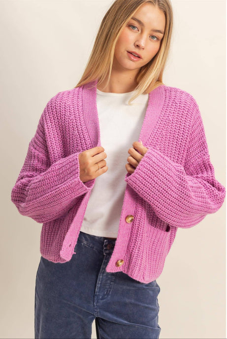 Woman wearing a pink knitted cardigan over a white shirt and blue jeans on a beige background